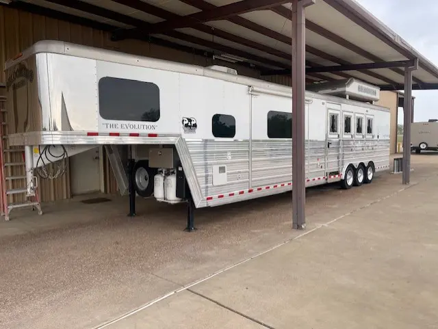 Large white horse trailer parked under a shelter.