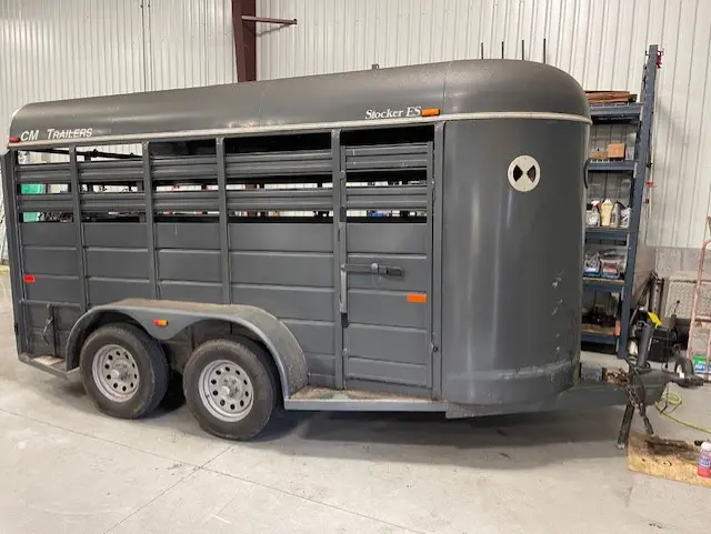 Gray metal livestock trailer parked indoors on a concrete floor.