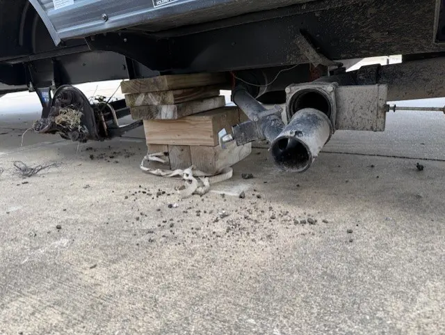 Car supported by wooden blocks and a tire undercarriage on rough ground.