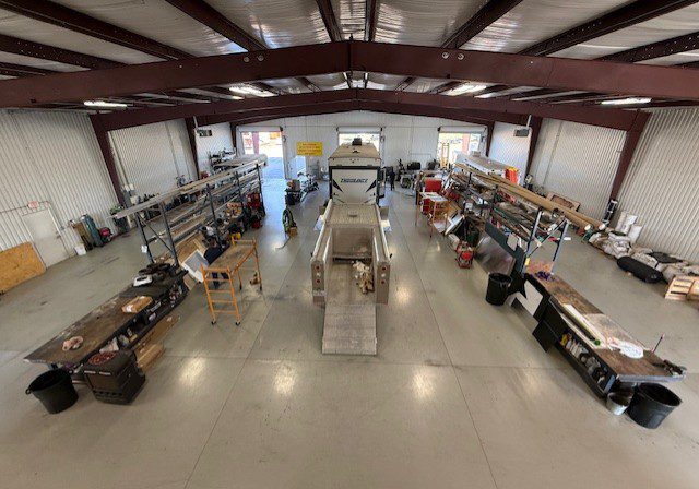 A spacious workshop with tools and equipment along the sides and a vehicle in the center.